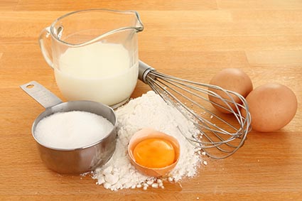 Ingredientes para hacer la masa, los huevos, la harina, la leche y el azúcar con una batidora en una encimera de madera,